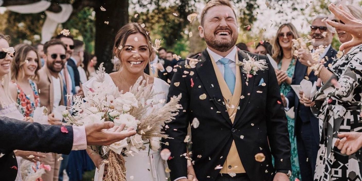 Mariés rayonnants sous une pluie de confettis naturels lors d’un mariage bohème en plein air.