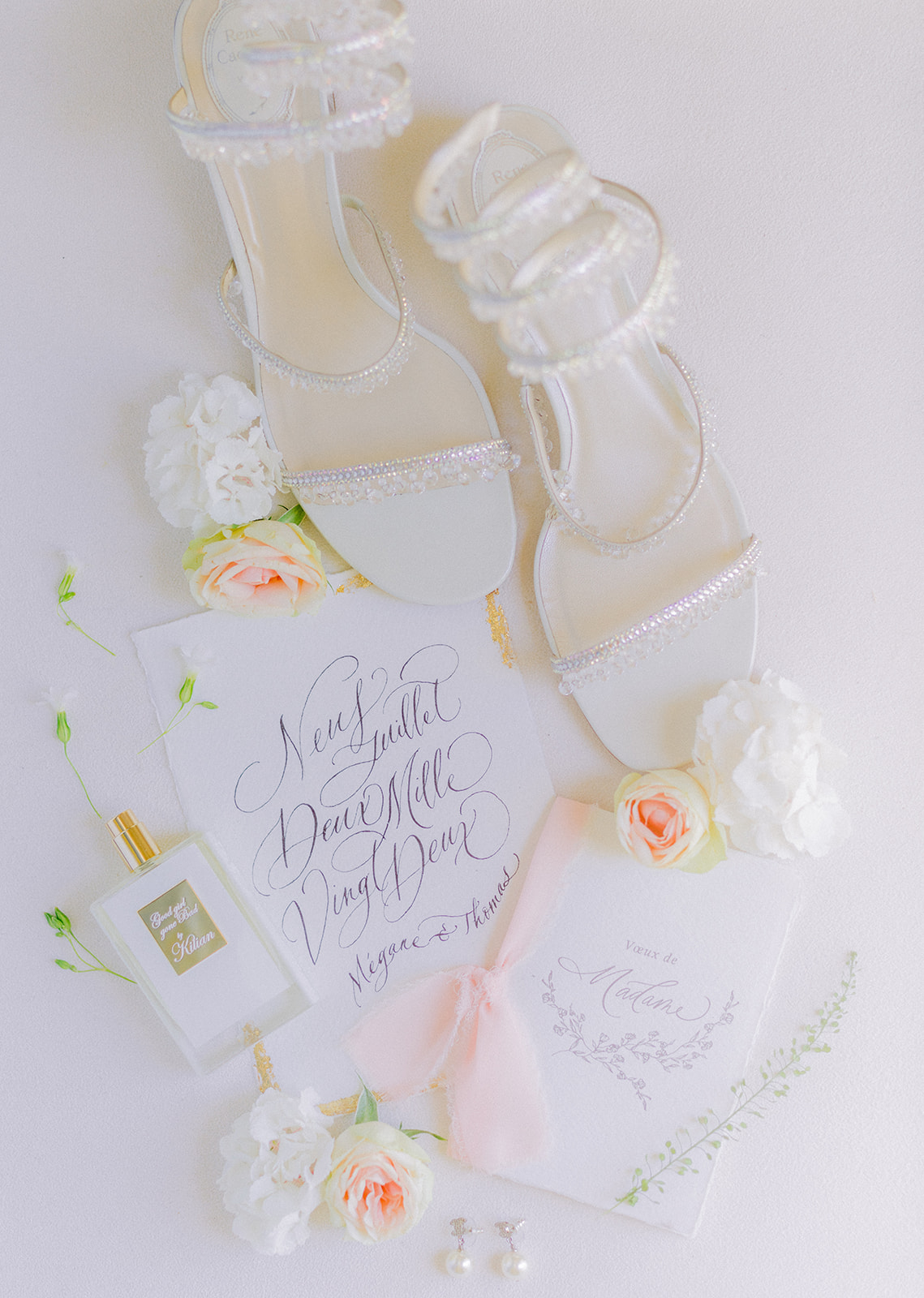 Accessoires de mariage : chaussures perlées, parfum de mariée, bijoux et faire-part décorés de fleurs.