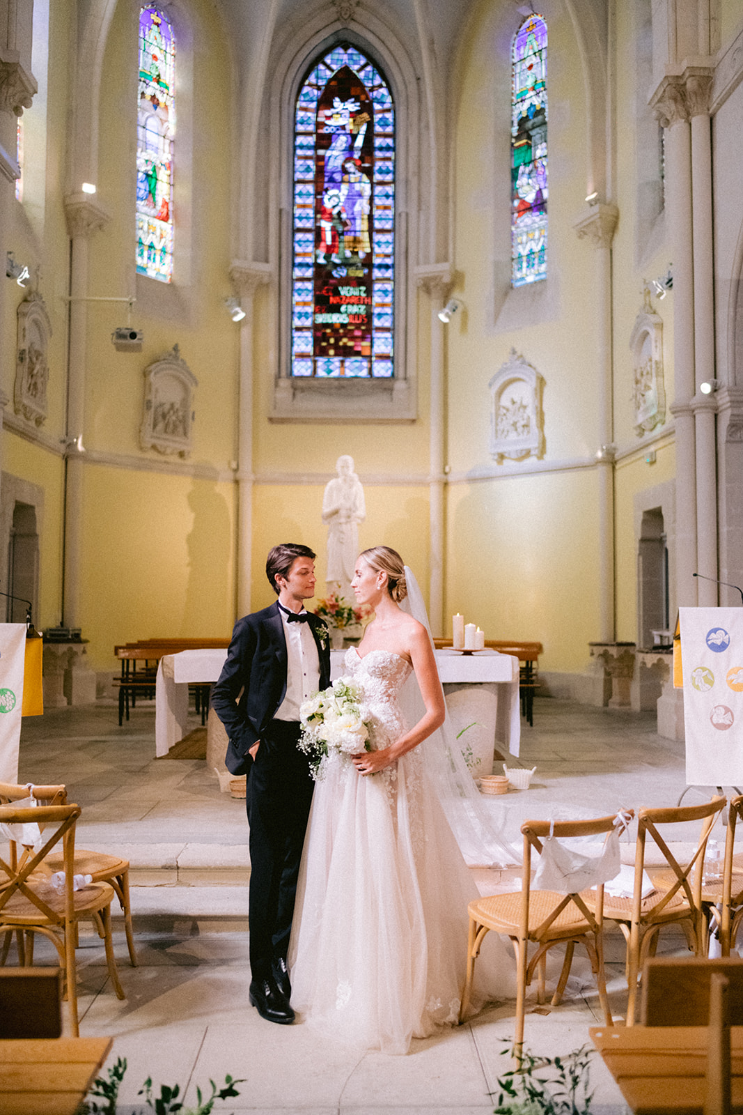 Photo des mariés devant l’autel d’une église, échange complice dans un décor majestueux et romantique.