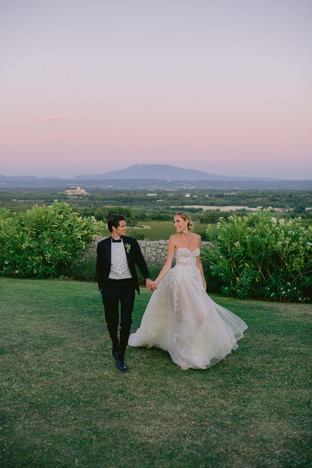 Photo romantique d’un couple de mariés marchant main dans la main pendant l’heure bleue, lumière magique du coucher de soleil.